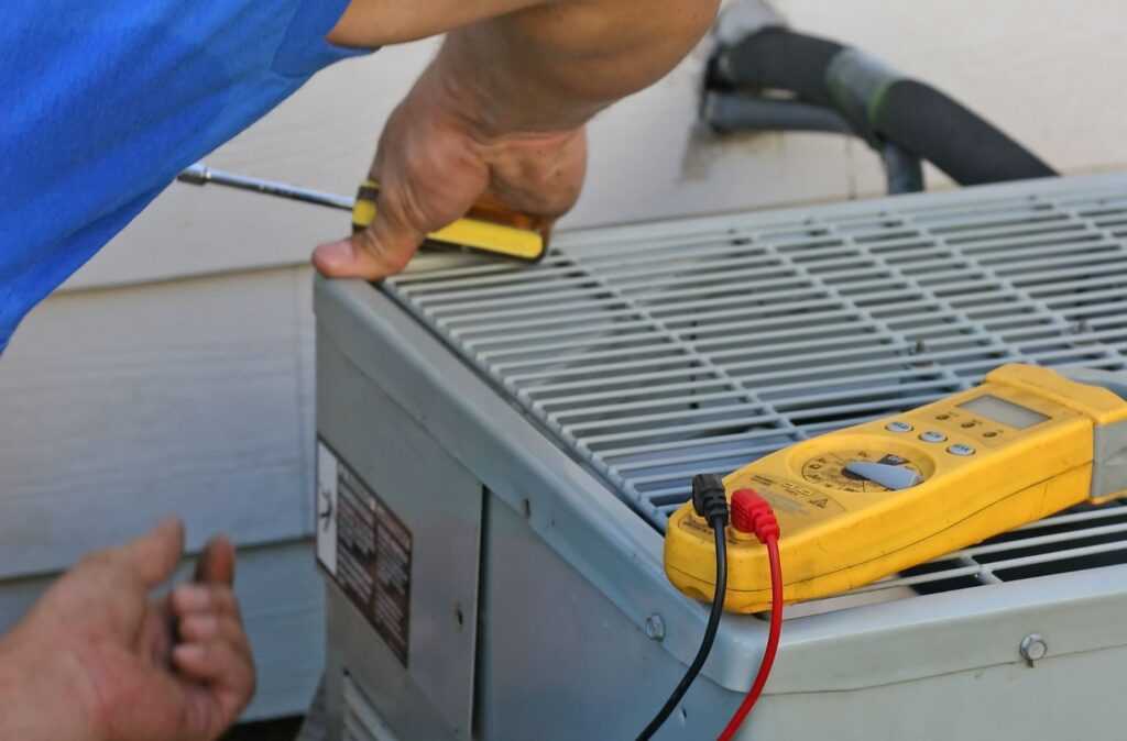 A technician is repairing an air conditioner, focused on the unit with tools in hand, in a well-lit environment.