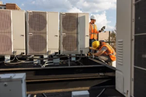 Two men collaborating on the maintenance of a large air conditioning unit outdoors.